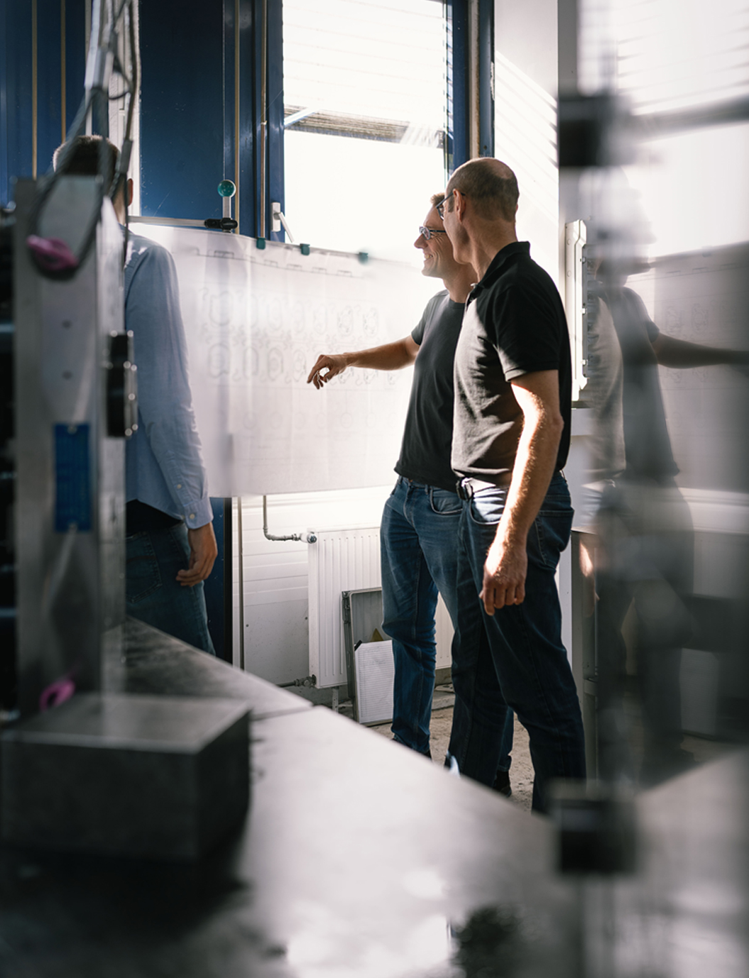 Zwei Mitarbeiter im Werkzeugbau besprechen einen Konstruktionsplott zur Planung der nächsten Arbeitsschritte in modernen Betriebsräumlichkeiten.